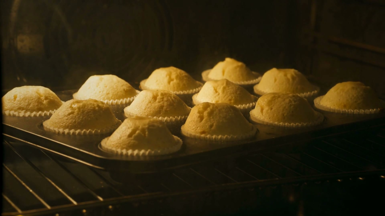Muffins rising and turning golden through an oven window
